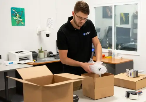A man packs a hard disk drive in anti-static wrap and a cardboard box for safe shipping.